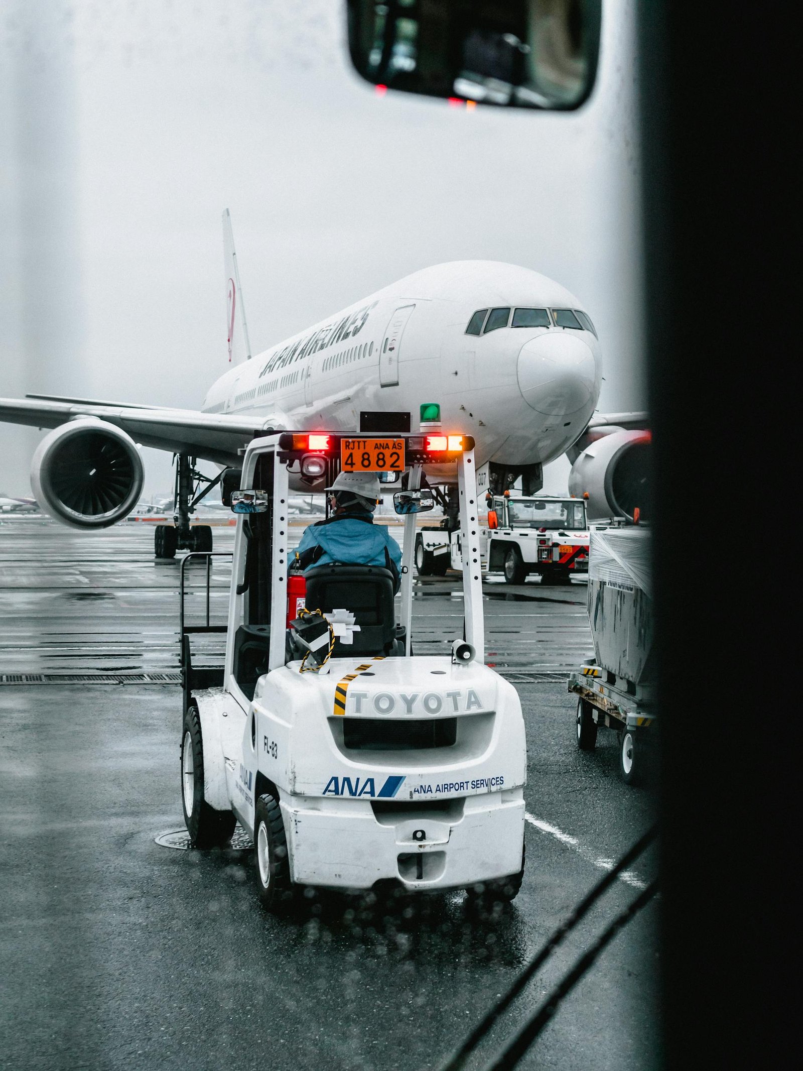 Airport ground crew operating a vehicle in front of a parked airliner on a rainy runway.