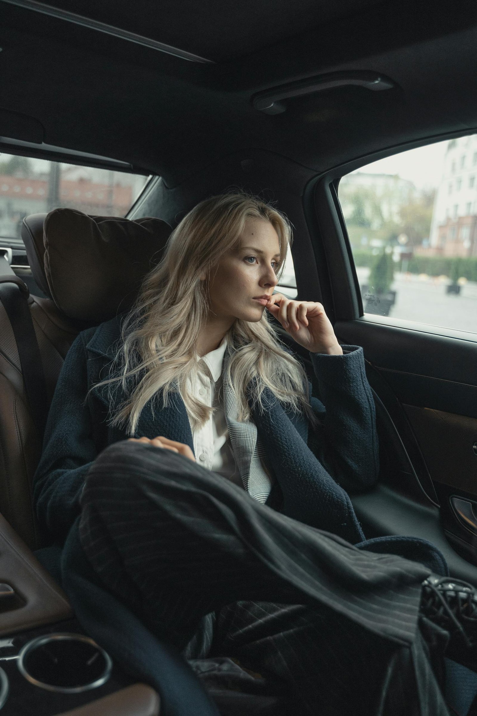 A thoughtful businesswoman sits in a luxurious car, pondering during a ride.