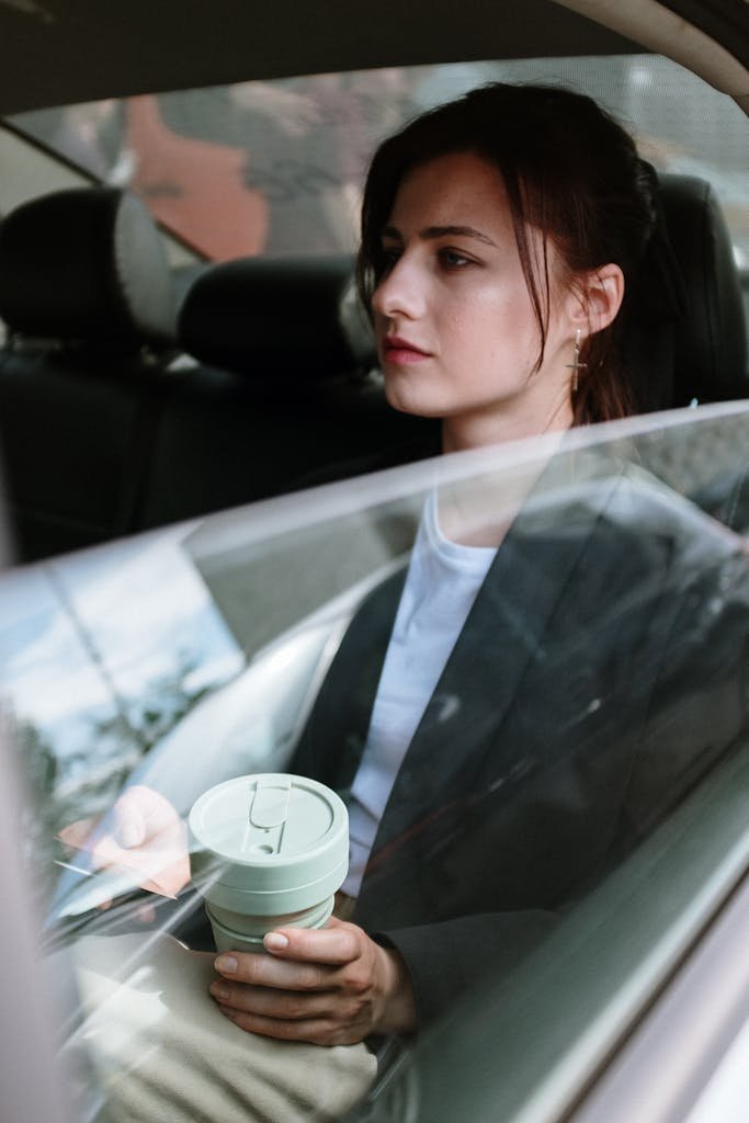 Thoughtful young woman holding coffee cup while commuting in car.